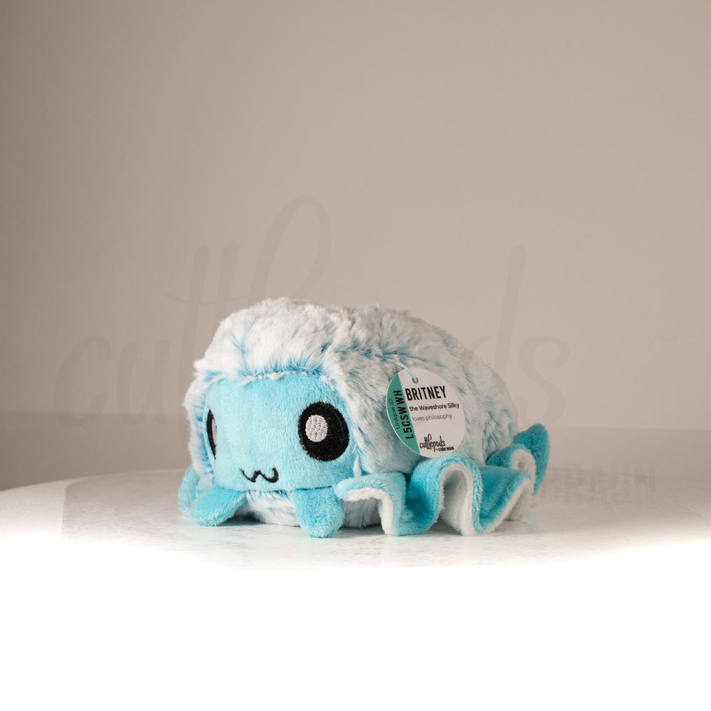 Front view of a cuttlepod plush toy, captured at a slight angle to highlight its charming features: large, cartoonish eyes, ruffled fins, and a cuddly, furry texture.