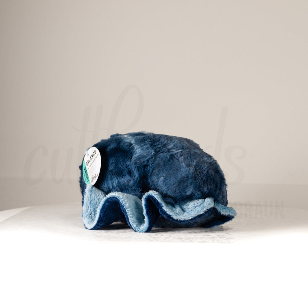 Slightly angled back view of a cuttlepod plush toy, highlighting two-tone ruffled fins, and a cuddly, furry body that comes to a soft point at the rear.