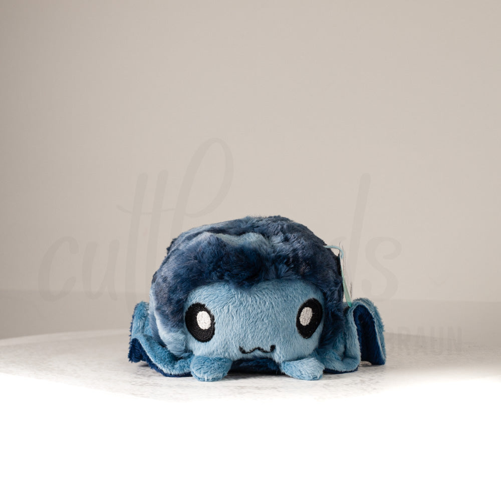 Front view of a cuttlepod plush toy, showcasing its unique form with large, cartoonish eyes, ruffled fins, and a cuddly, furry texture.