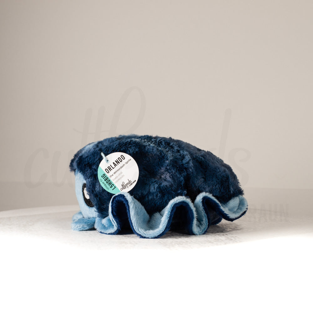 Side profile view of a cuttlepod plush toy, showcasing two-tone ruffled fins, and a cuddly, furry body.