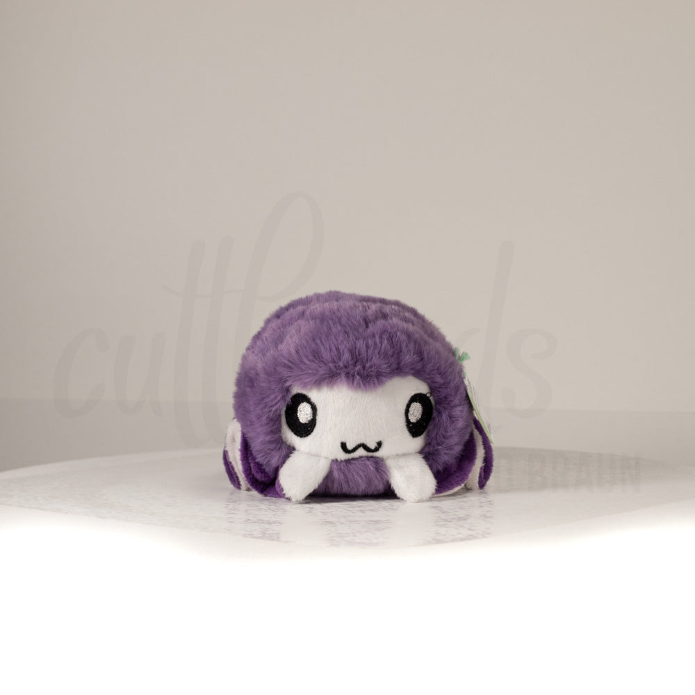 Front view of a cuttlepod plush toy, showcasing its unique form with large, cartoonish eyes, ruffled fins, and a cuddly, furry texture.