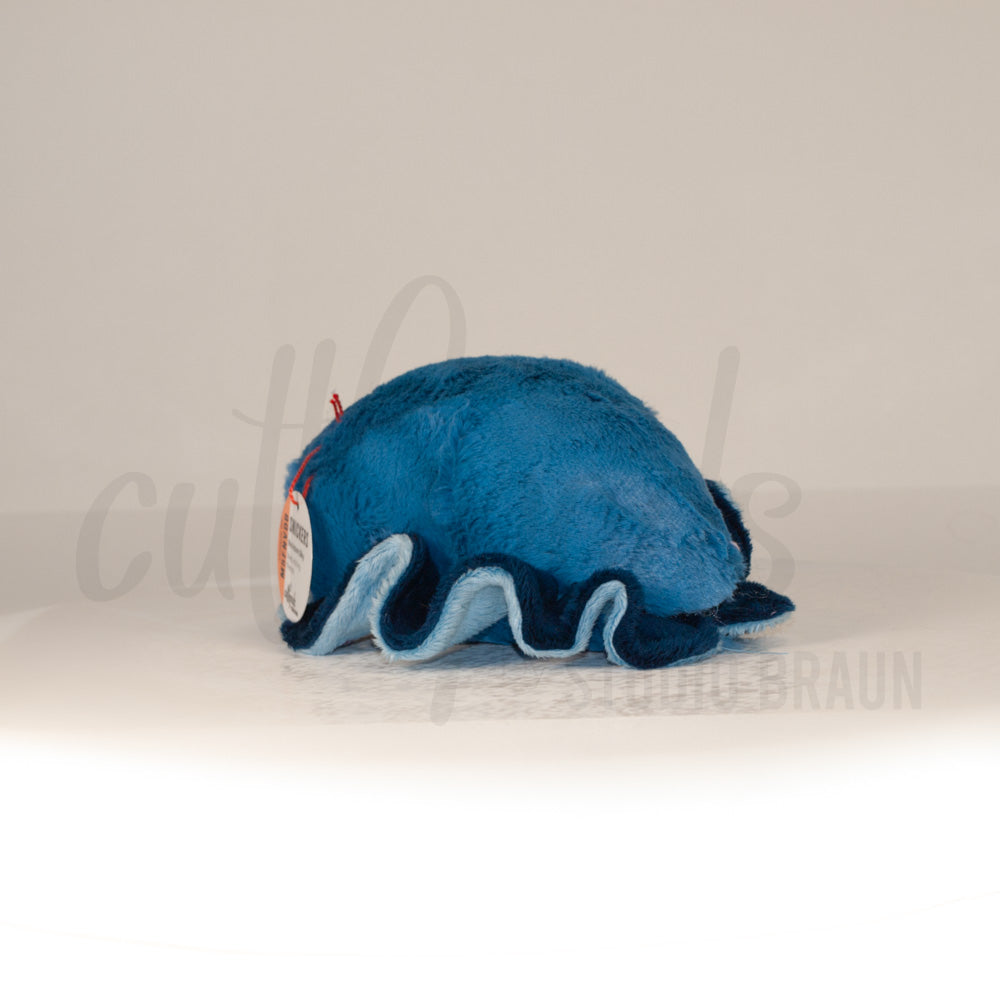 Slightly angled back view of a cuttlepod plush toy, highlighting two-tone ruffled fins, and a cuddly, furry body that comes to a soft point at the rear.