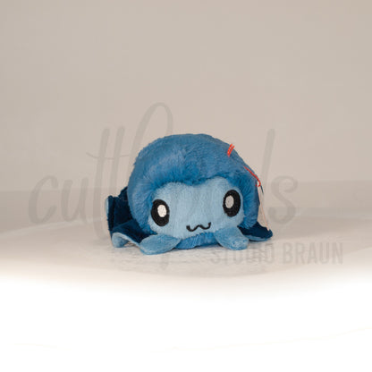 Front view of a cuttlepod plush toy, showcasing its unique form with large, cartoonish eyes, ruffled fins, and a cuddly, furry texture.