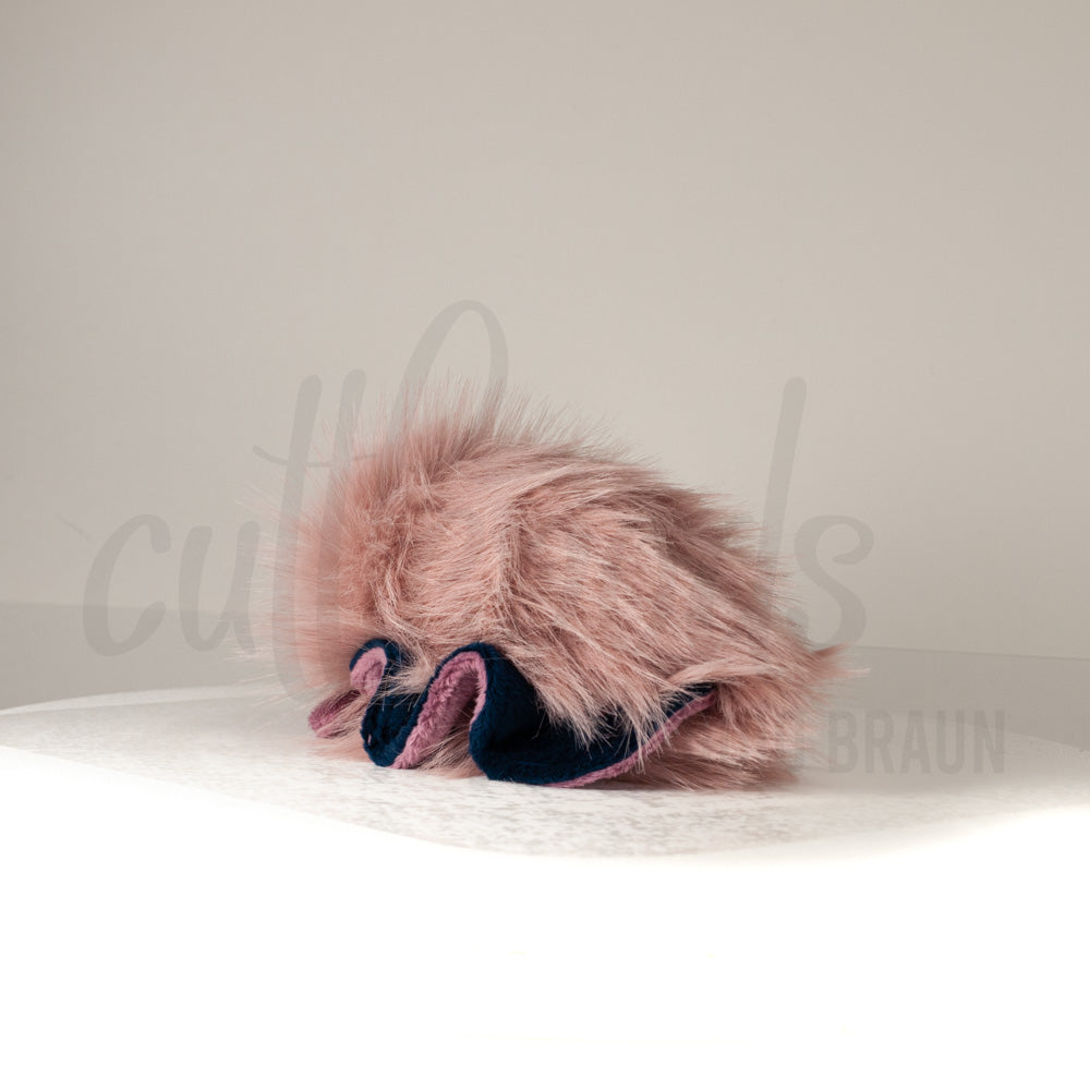 Slightly angled back view of a cuttlepod plush toy, highlighting two-tone ruffled fins, and a cuddly, furry body that comes to a soft point at the rear.