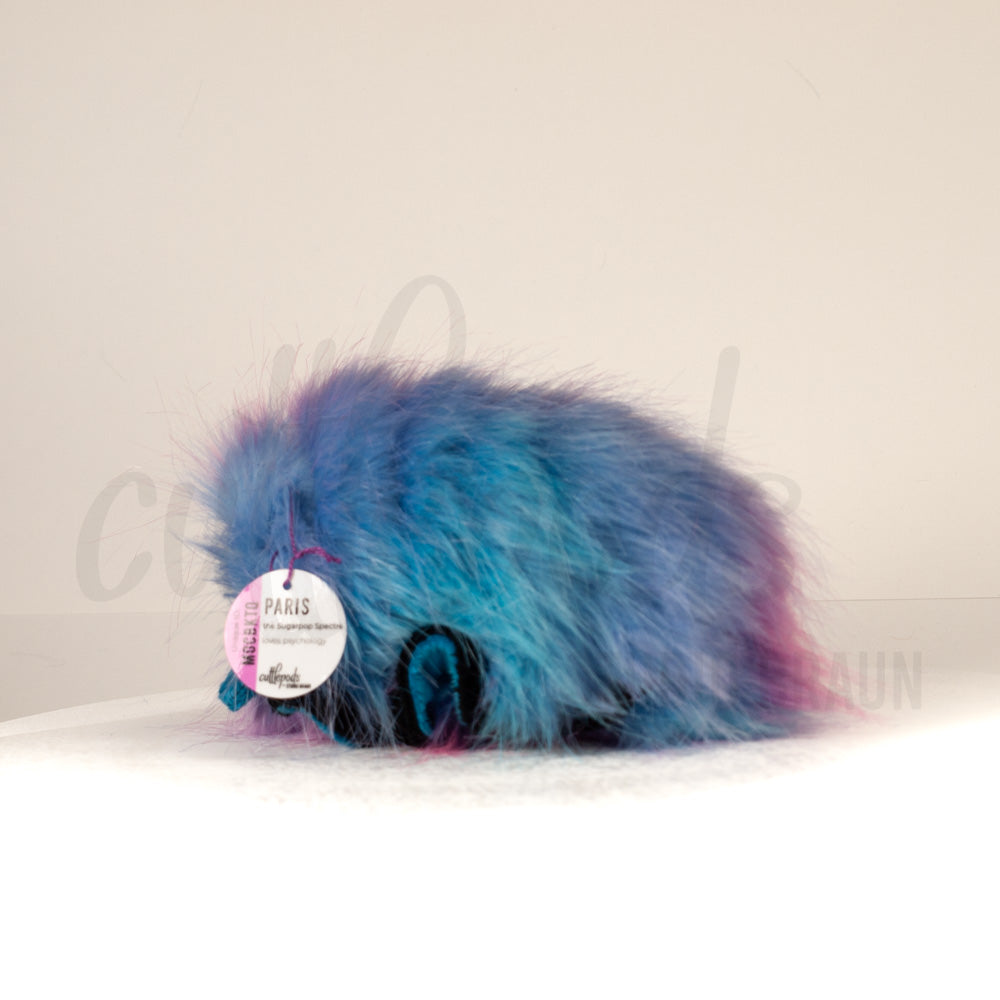 Slightly angled back view of a cuttlepod plush toy, highlighting two-tone ruffled fins, and a cuddly, furry body that comes to a soft point at the rear.