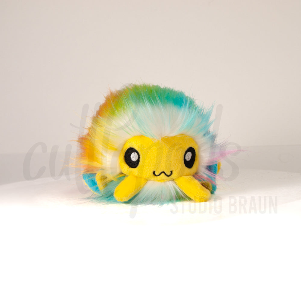 Front view of a cuttlepod plush toy, showcasing its unique form with large, cartoonish eyes, ruffled fins, and a cuddly, furry texture.