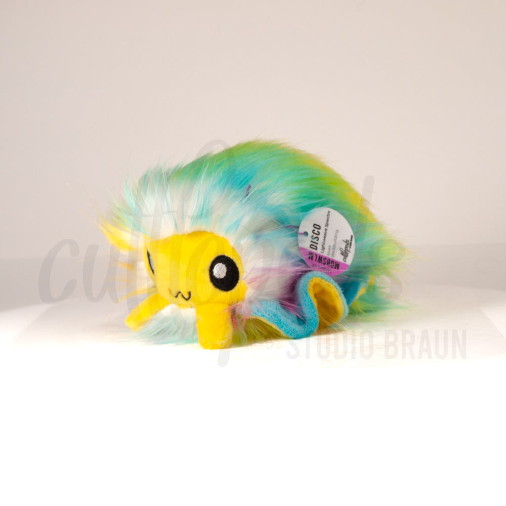 Front view of a cuttlepod plush toy, captured at a slight angle to highlight its charming features: large, cartoonish eyes, ruffled fins, and a cuddly, furry texture.