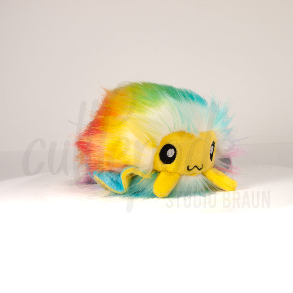 Front view of a cuttlepod plush toy, captured at a slight angle to highlight its charming features: large, cartoonish eyes, ruffled fins, and a cuddly, furry texture.