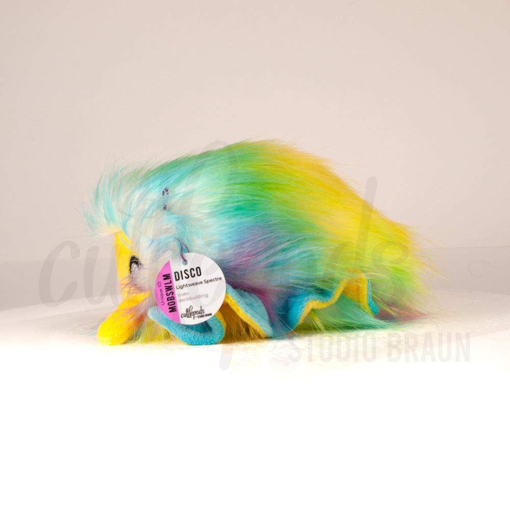 Side profile view of a cuttlepod plush toy, showcasing two-tone ruffled fins, and a cuddly, furry body.