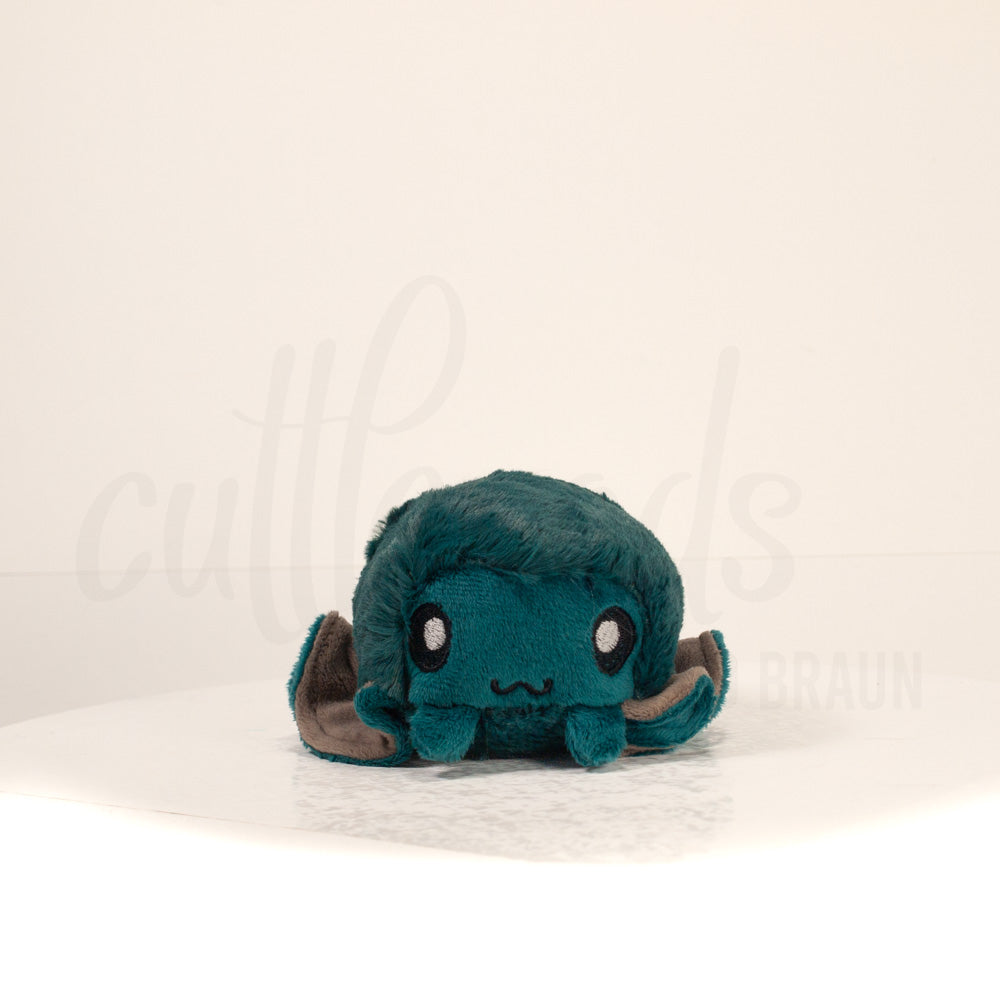 Front view of a cuttlepod plush toy, showcasing its unique form with large, cartoonish eyes, ruffled fins, and a cuddly, furry texture.