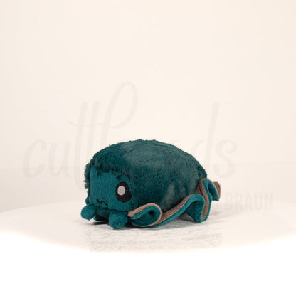 Front view of a cuttlepod plush toy, captured at a slight angle to highlight its charming features: large, cartoonish eyes, ruffled fins, and a cuddly, furry texture.