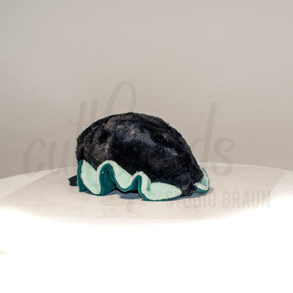 Slightly angled back view of a cuttlepod plush toy, highlighting two-tone ruffled fins, and a cuddly, furry body that comes to a soft point at the rear.