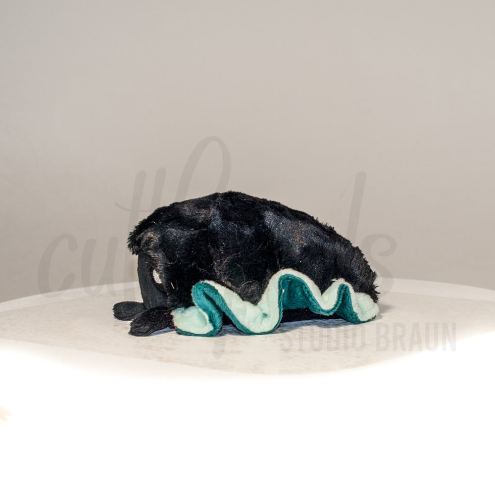 Side profile view of a cuttlepod plush toy, showcasing two-tone ruffled fins, and a cuddly, furry body.