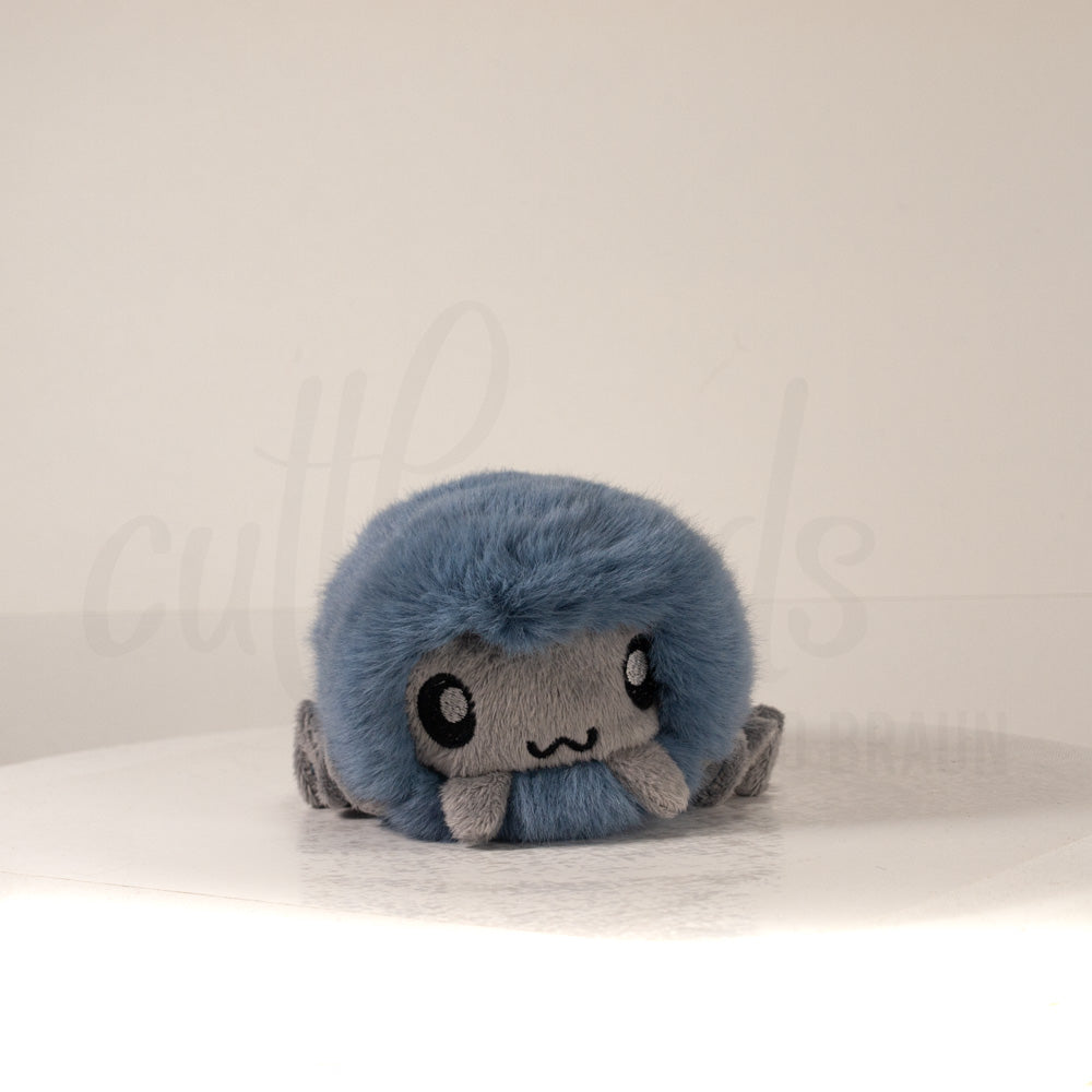 Front view of a cuttlepod plush toy, showcasing its unique form with large, cartoonish eyes, ruffled fins, and a cuddly, furry texture.