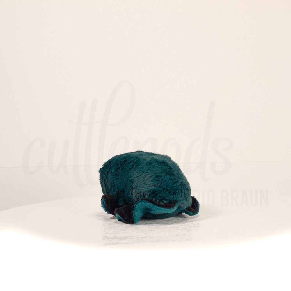 Slightly angled back view of a cuttlepod plush toy, highlighting two-tone ruffled fins, and a cuddly, furry body that comes to a soft point at the rear.