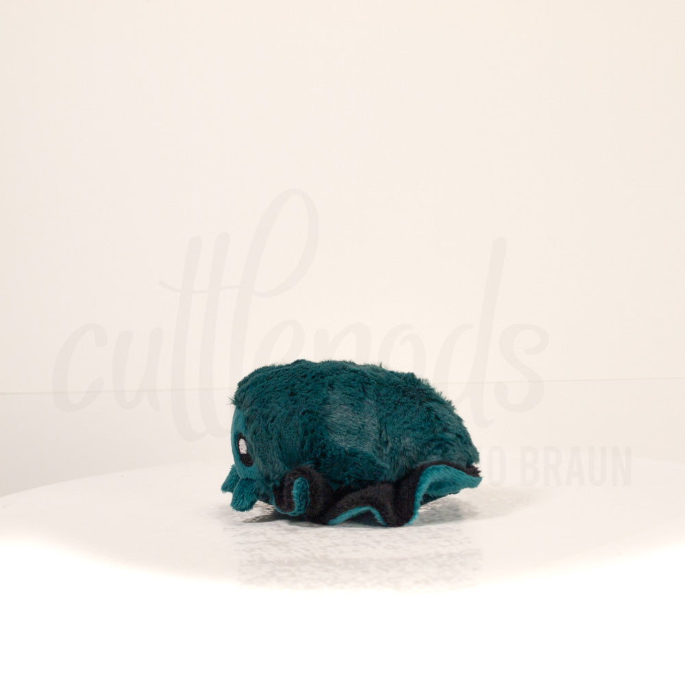 Side profile view of a cuttlepod plush toy, showcasing two-tone ruffled fins, and a cuddly, furry body.