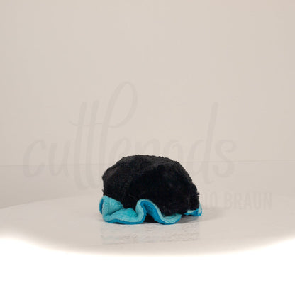 Slightly angled back view of a cuttlepod plush toy, highlighting two-tone ruffled fins, and a cuddly, furry body that comes to a soft point at the rear.