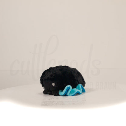 Front view of a cuttlepod plush toy, captured at a slight angle to highlight its charming features: large, cartoonish eyes, ruffled fins, and a cuddly, furry texture.