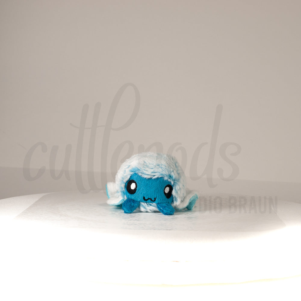 Front view of a cuttlepod plush toy, showcasing its unique form with large, cartoonish eyes, ruffled fins, and a cuddly, furry texture.