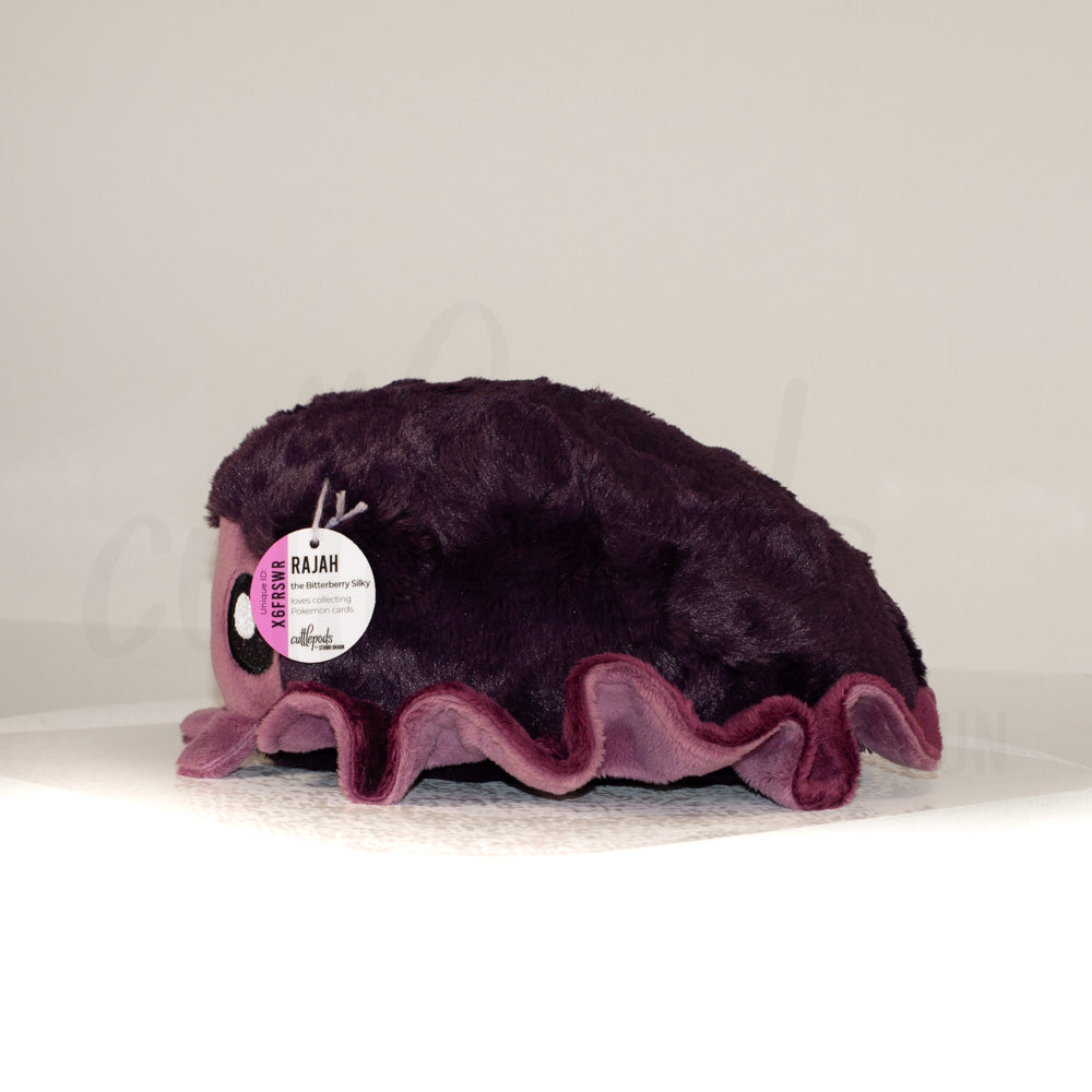 Side profile view of a cuttlepod plush toy, showcasing two-tone ruffled fins, and a cuddly, furry body.