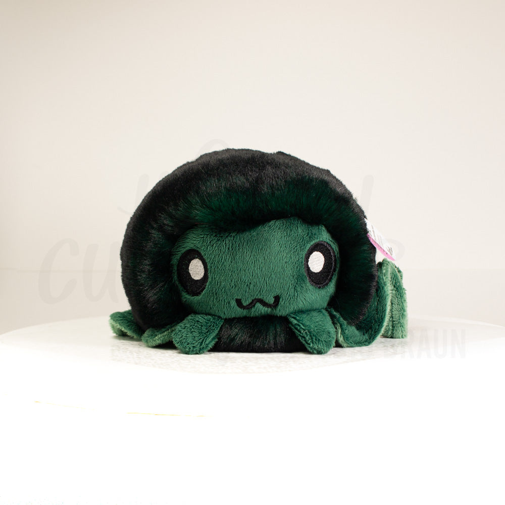 Front view of a cuttlepod plush toy, showcasing its unique form with large, cartoonish eyes, ruffled fins, and a cuddly, furry texture.