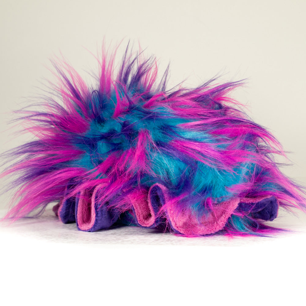 Slightly angled back view of a cuttlepod plush toy, highlighting two-tone ruffled fins, and a cuddly, furry body that comes to a soft point at the rear.