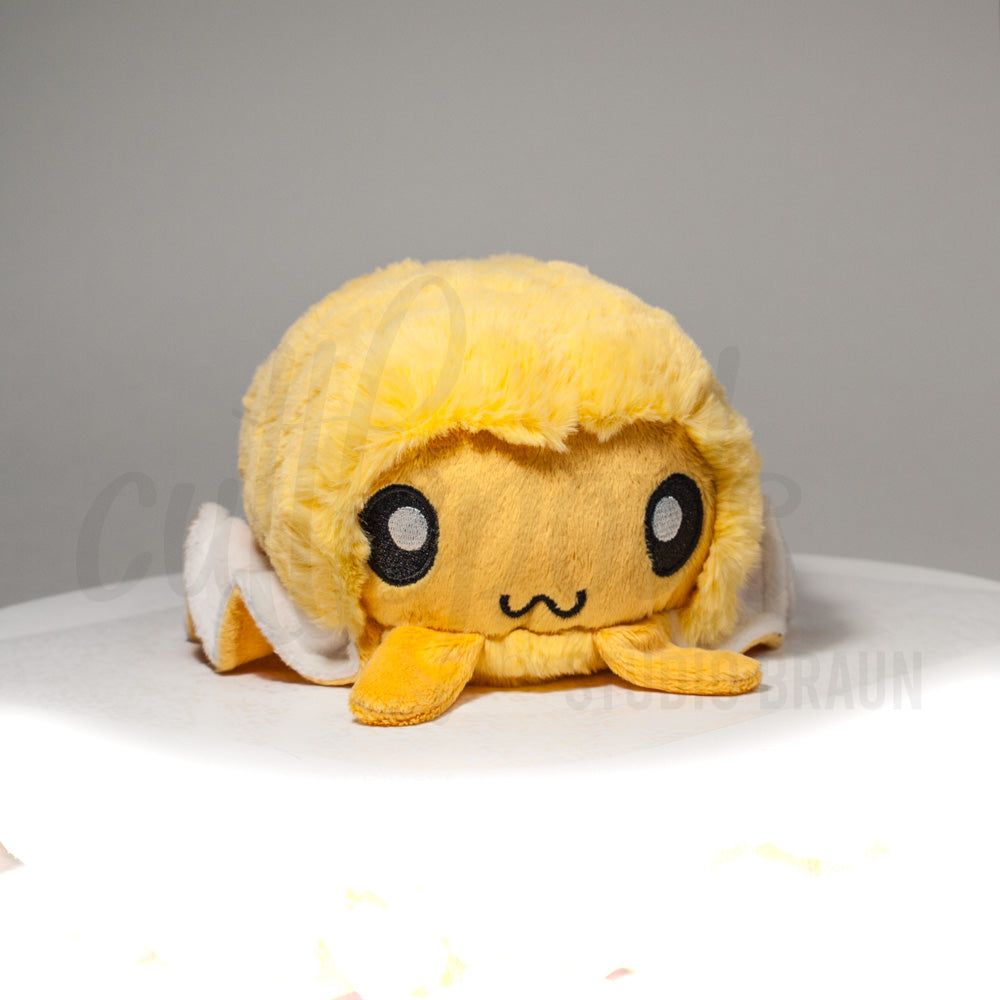 Front view of a cuttlepod plush toy, showcasing its unique form with large, cartoonish eyes, ruffled fins, and a cuddly, furry texture.