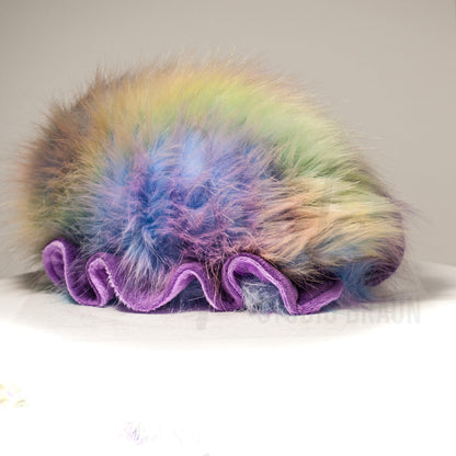 Slightly angled back view of a cuttlepod plush toy, highlighting two-tone ruffled fins, and a cuddly, furry body that comes to a soft point at the rear.