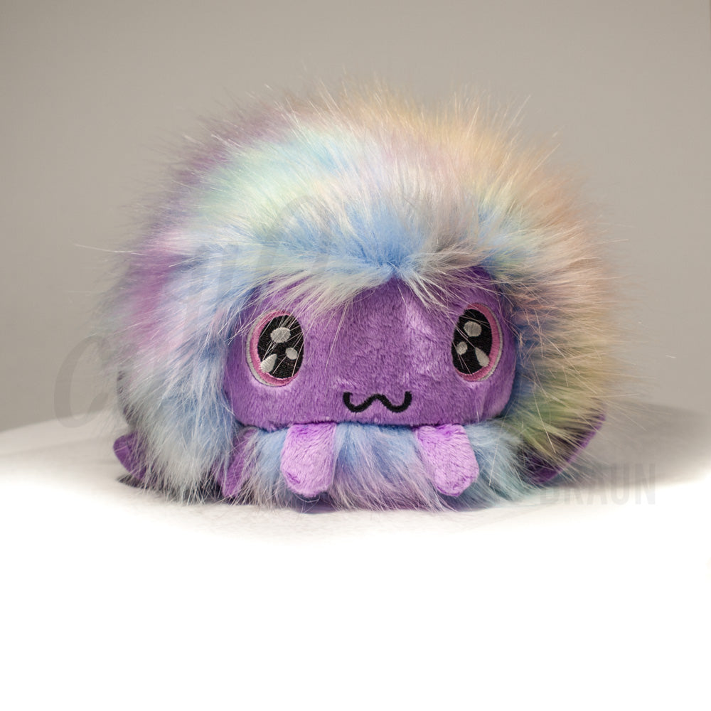 Front view of a cuttlepod plush toy, showcasing its unique form with large, cartoonish eyes, ruffled fins, and a cuddly, furry texture.