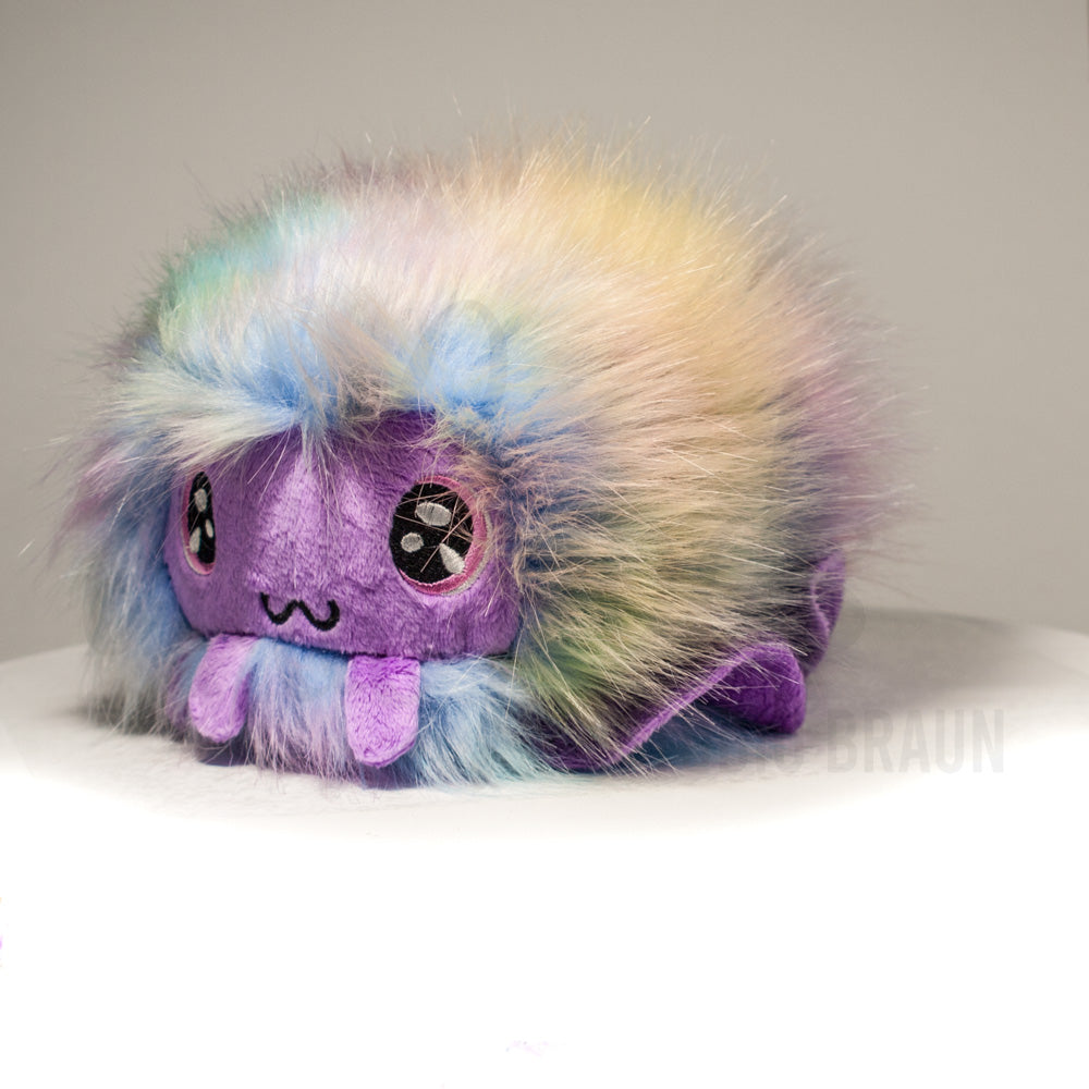 Front view of a cuttlepod plush toy, captured at a slight angle to highlight its charming features: large, cartoonish eyes, ruffled fins, and a cuddly, furry texture.