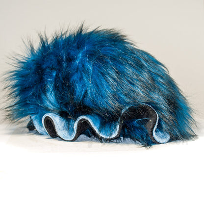 Slightly angled back view of a cuttlepod plush toy, highlighting two-tone ruffled fins, and a cuddly, furry body that comes to a soft point at the rear.