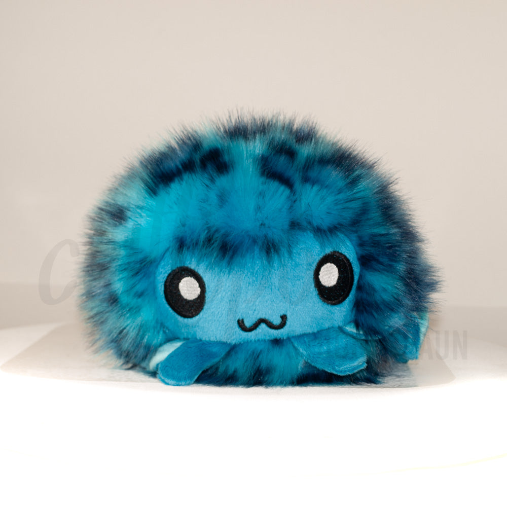 Front view of a cuttlepod plush toy, showcasing its unique form with large, cartoonish eyes, ruffled fins, and a cuddly, furry texture.