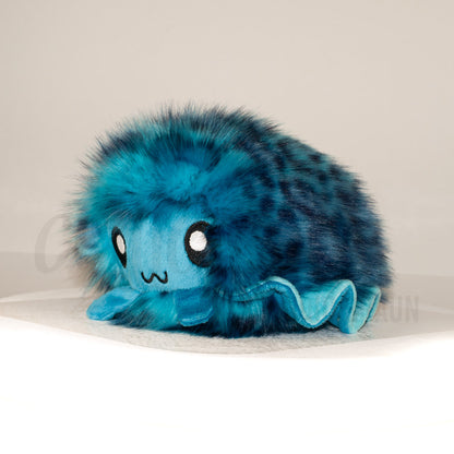 Front view of a cuttlepod plush toy, captured at a slight angle to highlight its charming features: large, cartoonish eyes, ruffled fins, and a cuddly, furry texture.