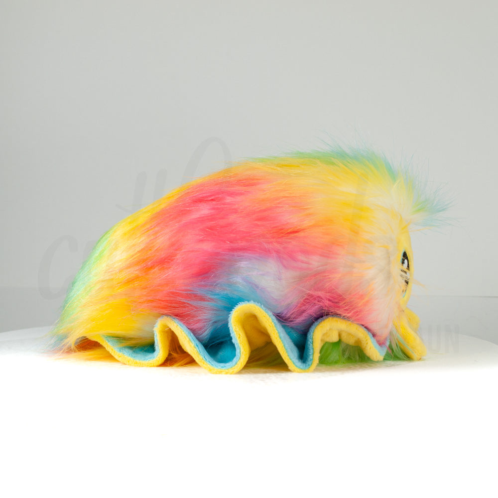 Side profile view of a cuttlepod plush toy, showcasing two-tone ruffled fins, and a cuddly, furry body.