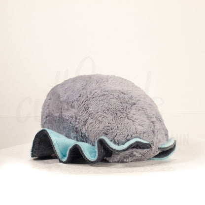 Slightly angled back view of a cuttlepod plush toy, highlighting two-tone ruffled fins, and a cuddly, furry body that comes to a soft point at the rear.