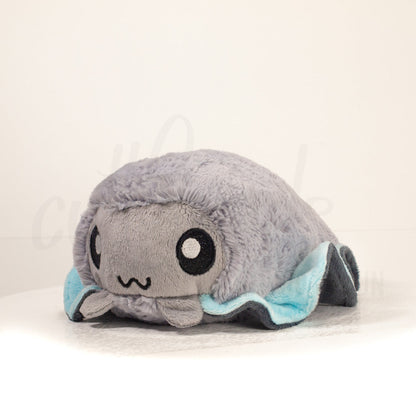 Front view of a cuttlepod plush toy, captured at a slight angle to highlight its charming features: large, cartoonish eyes, ruffled fins, and a cuddly, furry texture.