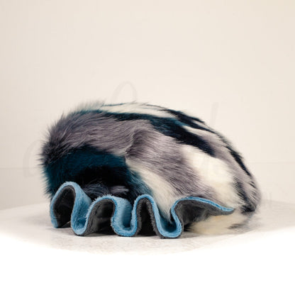 Slightly angled back view of a cuttlepod plush toy, highlighting two-tone ruffled fins, and a cuddly, furry body that comes to a soft point at the rear.