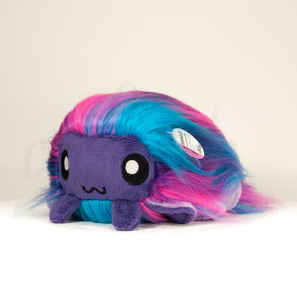 Slightly angled back view of a cuttlepod plush toy, highlighting two-tone ruffled fins, and a cuddly, furry body that comes to a soft point at the rear.