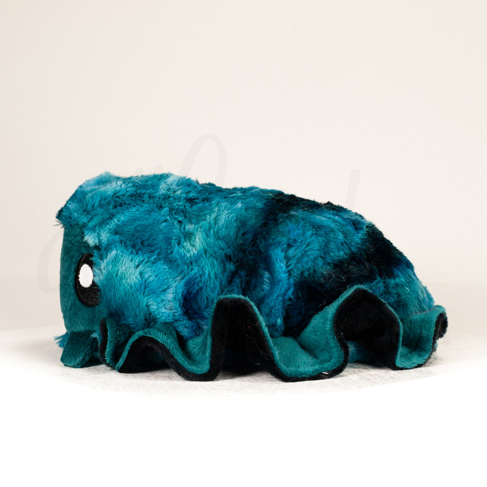 Side profile view of a cuttlepod plush toy, showcasing two-tone ruffled fins, and a cuddly, furry body.