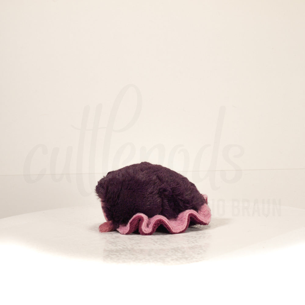 Side profile view of a cuttlepod plush toy, showcasing two-tone ruffled fins, and a cuddly, furry body.